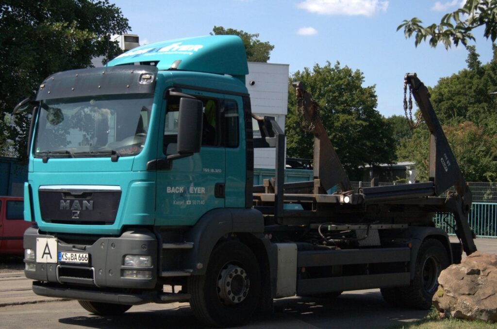 ein blauer Absetz-LKW der grade einen blauen Container absetzt